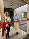 To kvinner klipper en rød snor ved inngangen til et nytt bygg.
