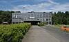 Moderne kontorbygg med glassfasade ved en grusvei, omgitt av grøntområde og skog.