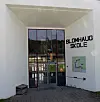 Hvitt skolebygg med stor inngang, glassdører og skiltet Blomhaug skole på veggen.