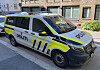 Norsk politibil parkert ved fortauet foran en murbygning.
