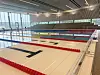 Stort innendørs svømmebasseng med røde banetau i en lys hall.