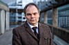 Tore Frellumstad står på en gangbro med bybygninger og metallrekkverk i bakgrunnen.