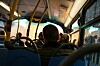 Sett bakfra av busspassasjerer i et opplyst kjøretøy med vinduer mot gaten utenfor.