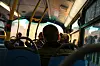 Sett bakfra av busspassasjerer i et opplyst kjøretøy med vinduer mot gaten utenfor.