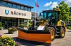 En gul traktor med stor snøplog står foran et rådhus med norsk flagg.