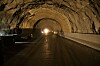 Innvendig i en mørk tunnel med våt vei, buet tak og sterkt lys langt fremme.