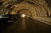 Innvendig i en mørk tunnel med våt vei, buet tak og sterkt lys langt fremme.