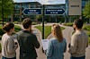 Fire personer står foran to veiskilt som viser «Ordinær konkurranse» og «Reservert for ideelle § 30-2a» ved et rådhus.