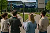 Fire personer står foran to veiskilt som viser «Ordinær konkurranse» og «Reservert for ideelle § 30-2a» ved et rådhus.