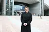 En kvinne i svart frakk står foran en moderne terminal med glassfasade.