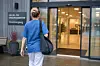 Person i blå helseuniform går mot glassdøren til et helse- og omsorgssenter.