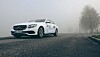 Hvit Mercedes-benz på en tåket vei med trær i bakgrunnen.