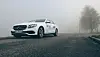 Hvit Mercedes-benz på en tåket vei med trær i bakgrunnen.