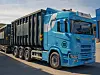 Blå Scania-lastebil med svart tilhenger står parkert ved veien.