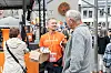Frivillige i oransje trøyer deler ut en pappeske til en mann i grå genser utendørs.