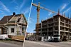 Et mindre rehabilitert bygg står ved siden av en større betongbygning under oppføring med en høy kran.