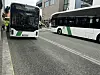 To hvite og grønne bybusser kjører på en bygate.