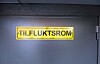 Gult tilfluktsromskilt på en mørkegrå metalldør.
