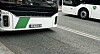Fronten av en hvit og grønn buss på en bygate, med en annen buss i bakgrunnen.