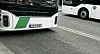 Fronten av en hvit og grønn buss på en bygate, med en annen buss i bakgrunnen.