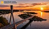 Skråkabelbru over en fjord ved solnedgang, med små øyer og oransje himmel.