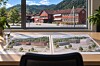 Arkitekturteikningar på eit bord framfor eit vindauge med raude bygningar og fjell i bakgrunnen.