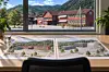 Arkitekturteikningar på eit bord framfor eit vindauge med raude bygningar og fjell i bakgrunnen.