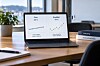 Laptop med diagrammer om pris og kvalitet på et skrivebord ved et vindu.