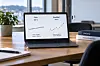 Laptop med diagrammer om pris og kvalitet på et skrivebord ved et vindu.