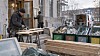 To personer arbeider med treverk og byggematerialer utenfor en bygning.
