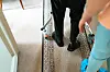 To personer ved en inngangsdør, med mønstret gulvløper og ganghjelpemidler.