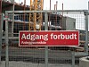 Rødt adgangsforbudsskilt på gjerde foran en byggeplass med gul kran.