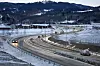 Biler på en svingete, snødekt vei med skogkledde åser i bakgrunnen.