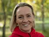 Smilende kvinne i rød jakke foran en uskarp grønn skog.
