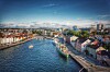 Flyfoto av en havn med fargerike trehus, båter og bybebyggelse langs vannet.