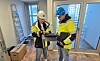 To arbeidere i hjelmer og verneklær arbeider sammen i et rom under oppussing.