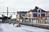 Snødekket jernbanestasjon med historisk murbygning, perronger og spor.