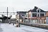 Snødekket jernbanestasjon med historisk murbygning, perronger og spor.